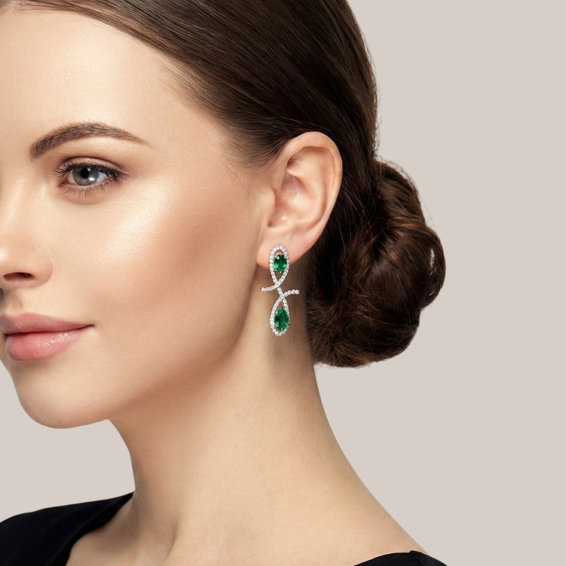 Close-up of a woman wearing green emerald earrings with a neutral background