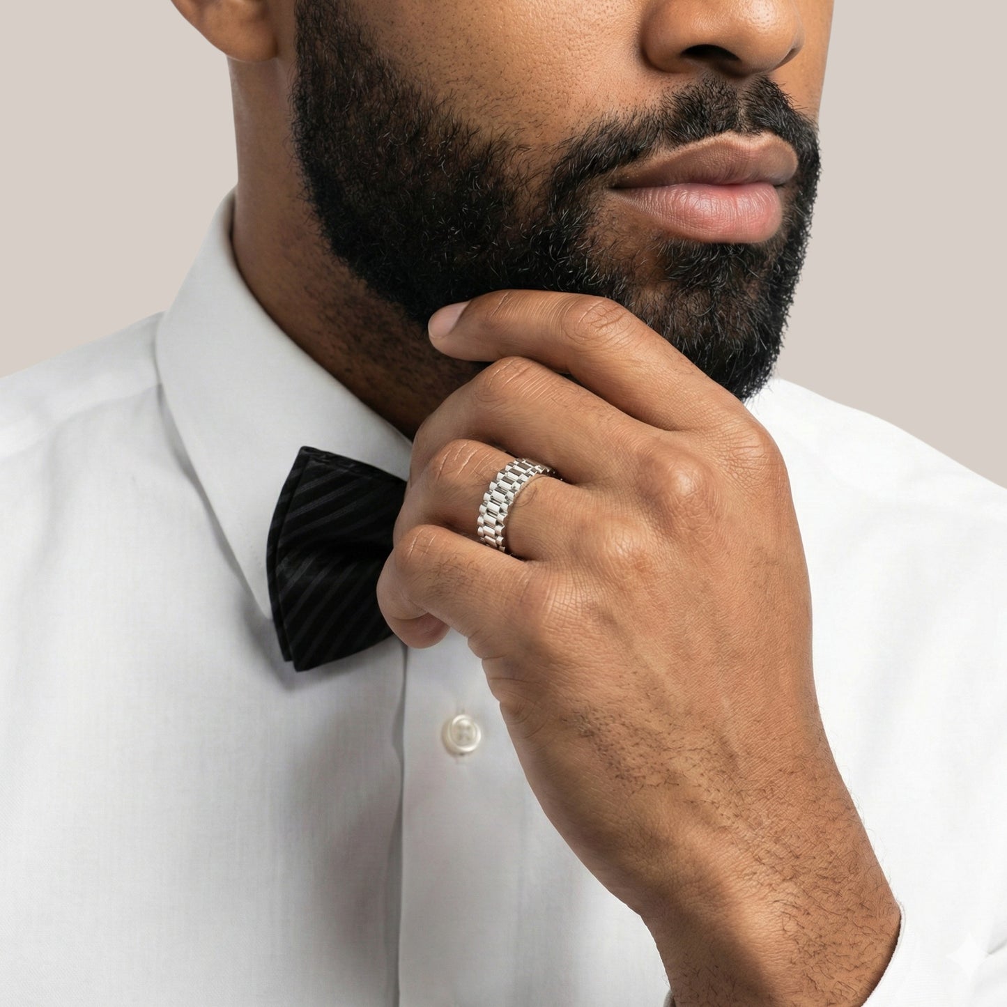 Man wearing a white shirt with a black bow tie, touching his chin.