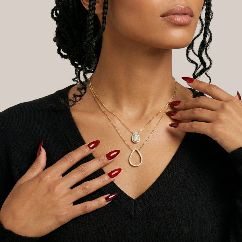 Woman wearing a gold necklace with a teardrop pendant, with a neutral background