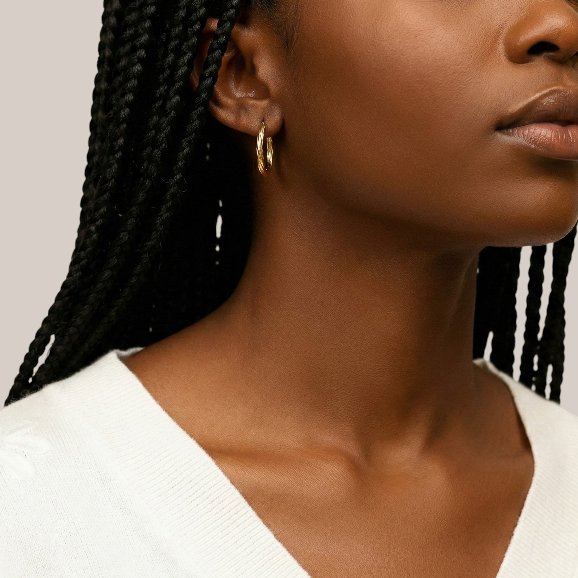 Close-up of a woman with braided hair wearing gold hoop earrings against a neutral background