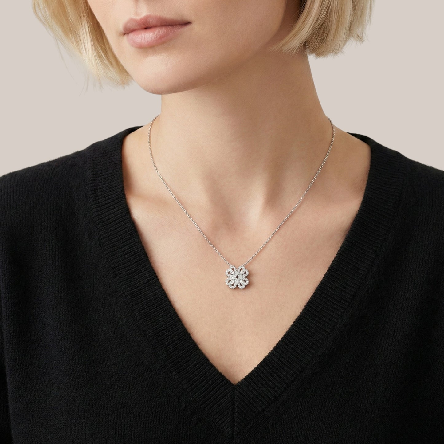 Person wearing a black sweater with a silver necklace featuring a clover pendant.