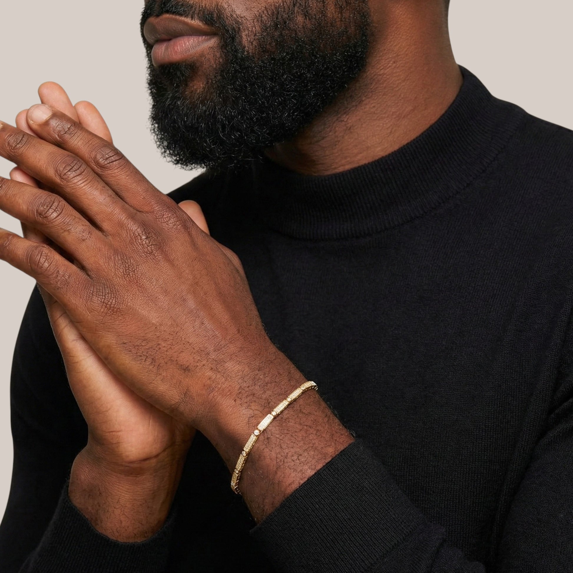 Man wearing a black turtleneck with a gold bracelet on his wrist, against a neutral background