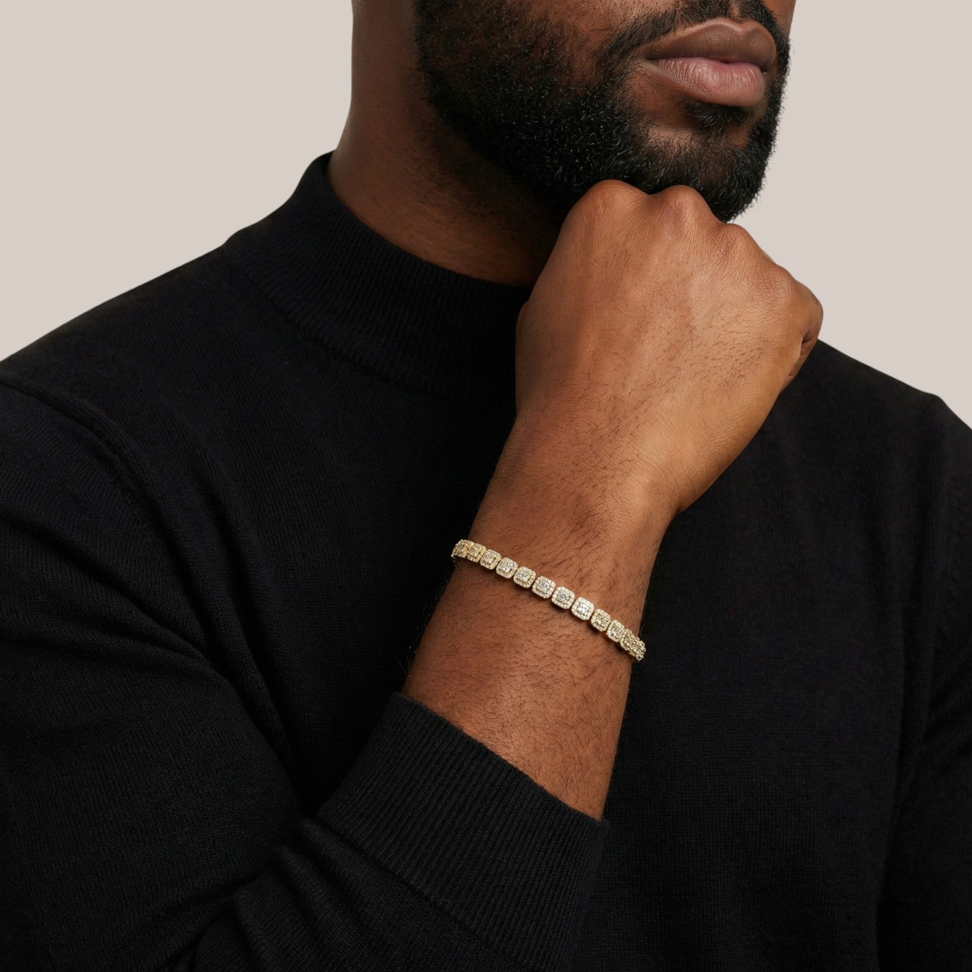 Man wearing a black sweater with a gold bracelet on a neutral background