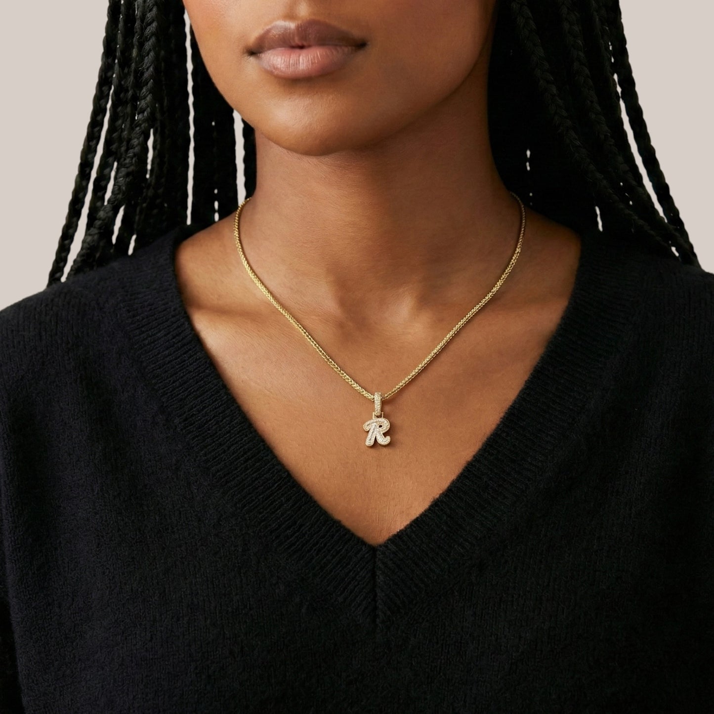 Woman wearing a gold necklace with a 'R' pendant against a neutral background