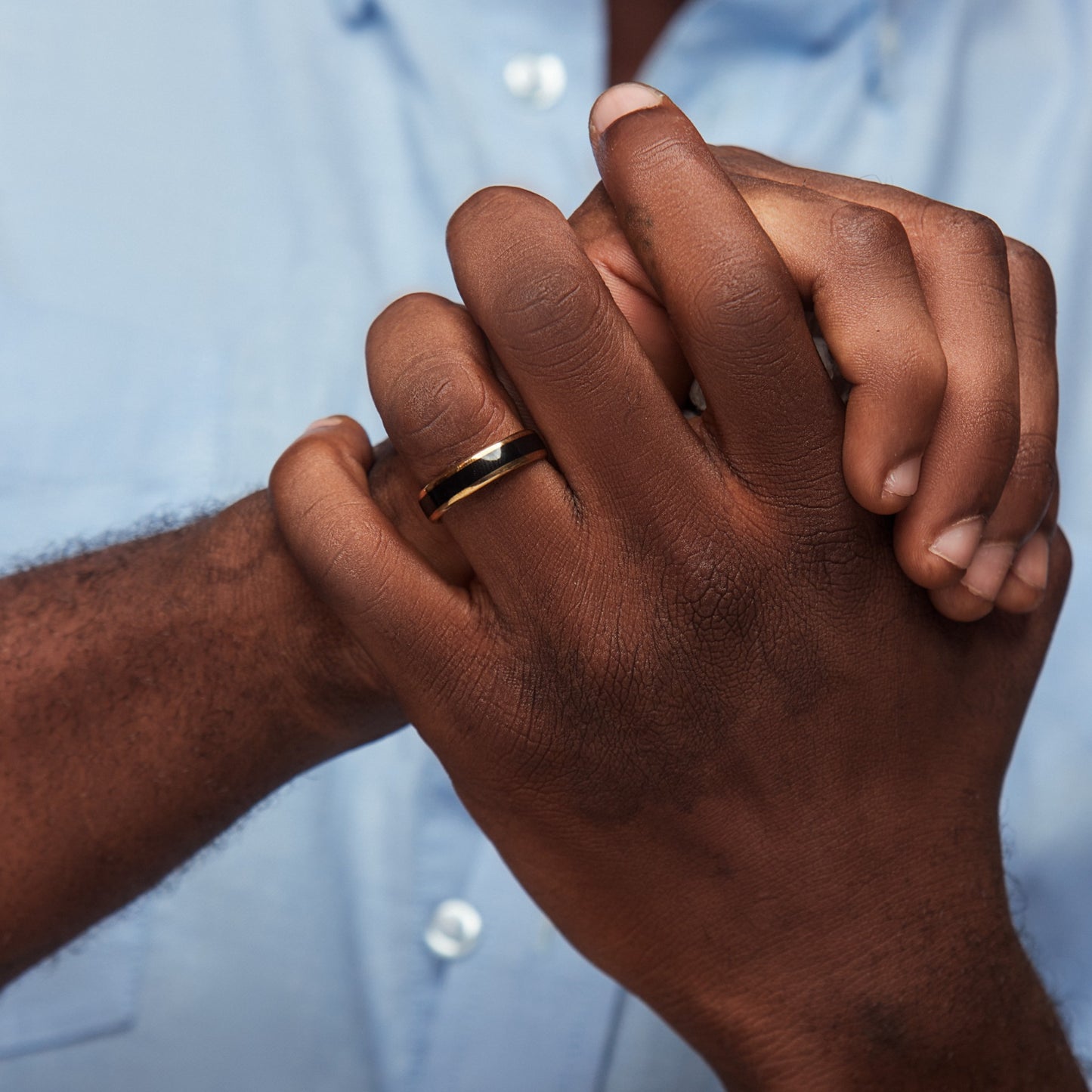 Close-up of two hands holding each other with a blurred light blue shirt in the background
