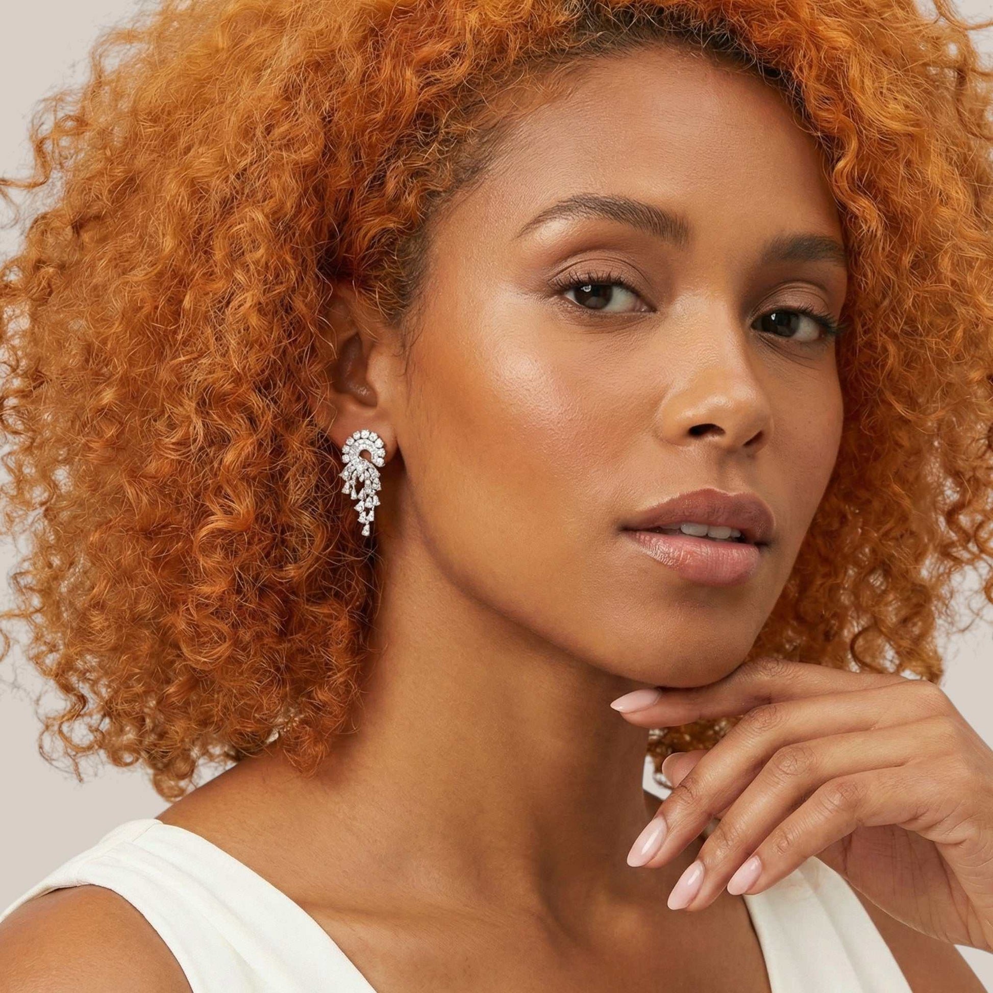 Woman with curly hair wearing a white top against a neutral background