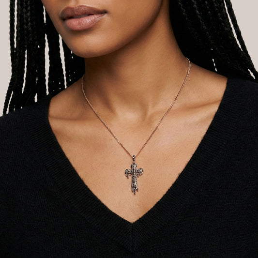 Close-up of a person wearing a necklace with a cross pendant against a neutral background