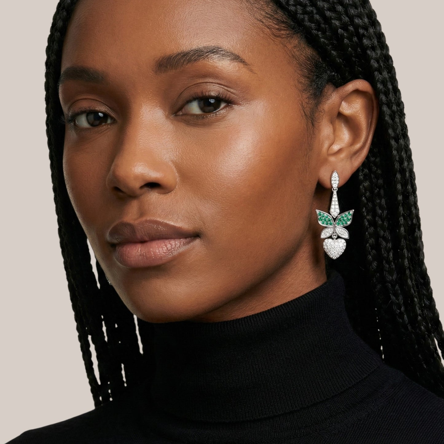 Close-up of a woman wearing butterfly earrings with green gemstones on a neutral background