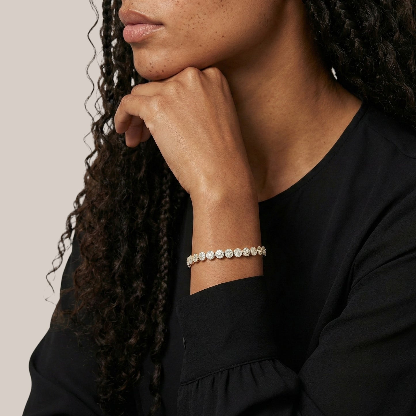 Woman wearing a black top with a bracelet on her wrist against a neutral background