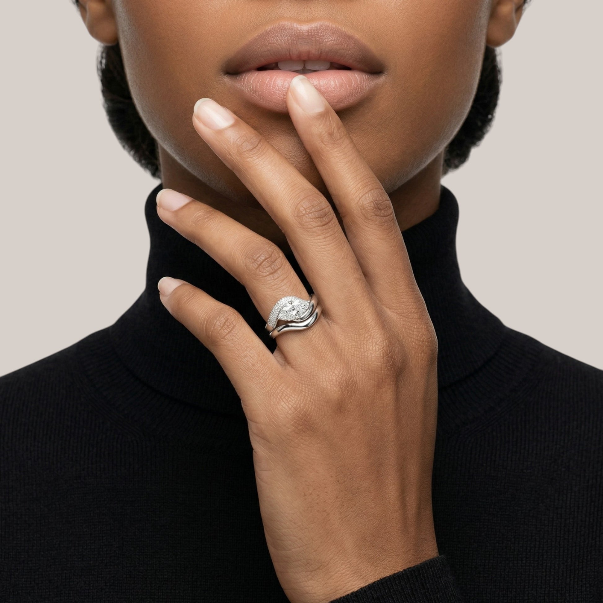 Close-up of a hand wearing a ring with a black turtleneck and neutral background