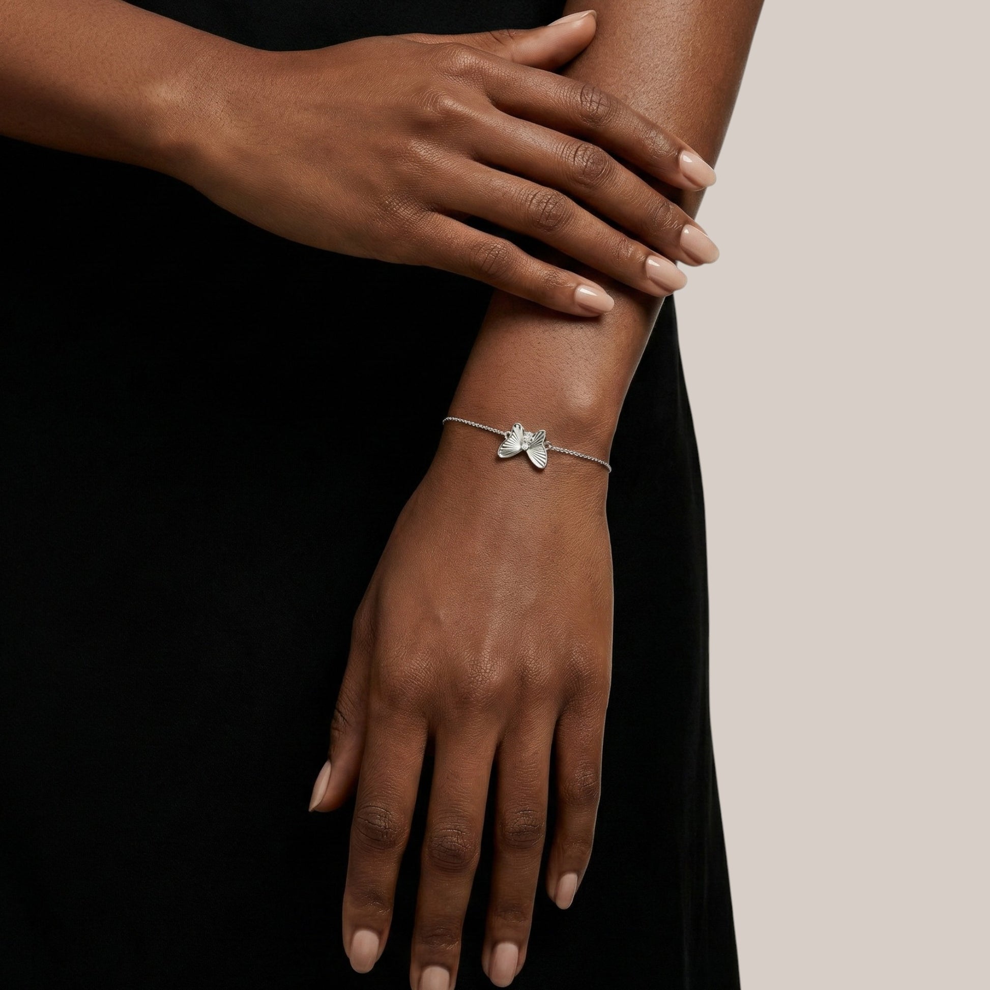 Silver bracelet with a butterfly design on a wrist against a neutral background