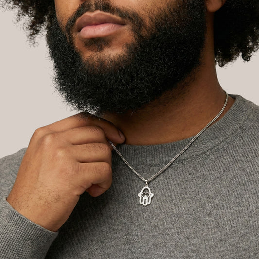 Man wearing a silver necklace with a Hamsa hand pendant against a neutral background