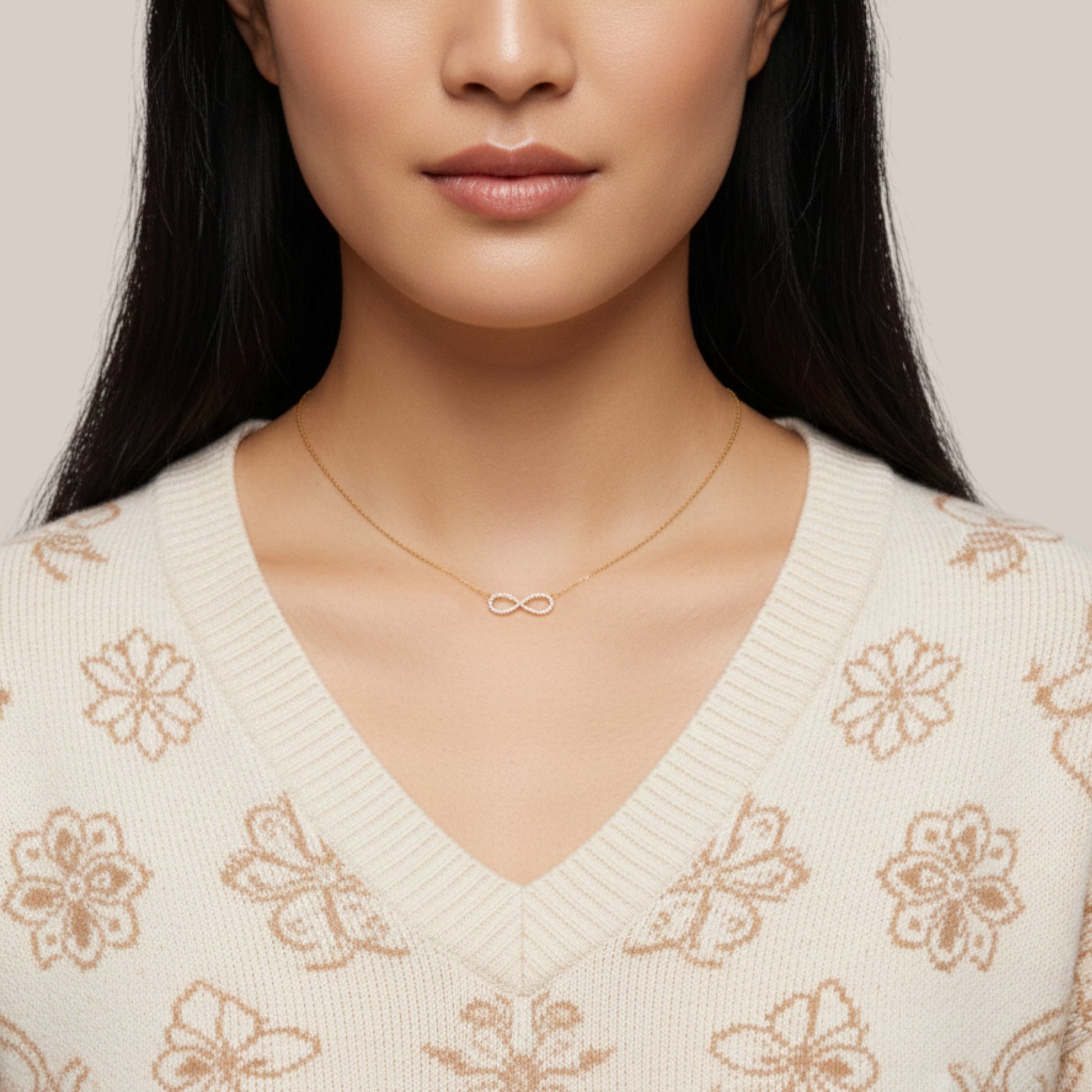 Woman wearing a gold necklace with an infinity symbol on a neutral background