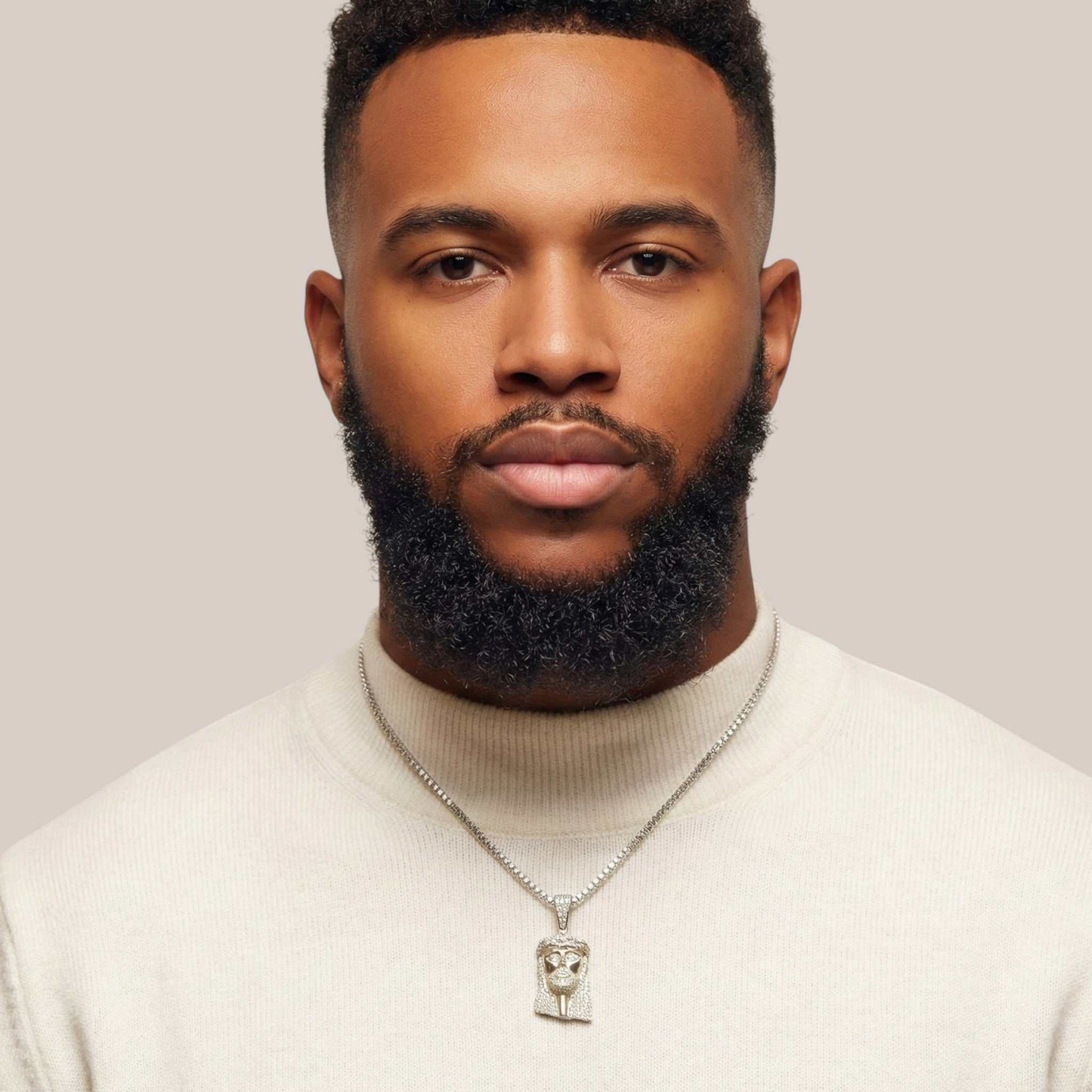 Man wearing a white sweater and silver necklace with a pendant against a plain background