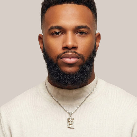 Man wearing a white sweater and silver necklace with a pendant against a plain background