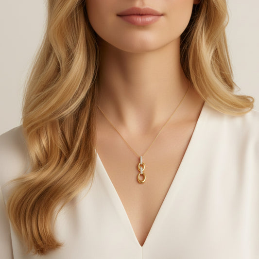 Close-up of a person wearing a gold necklace with a pendant against a neutral background