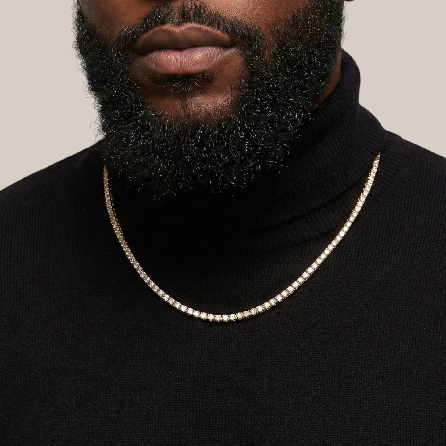 Man wearing a black turtleneck and gold chain necklace against a neutral background