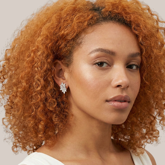 Woman with curly red hair wearing a white top against a neutral background