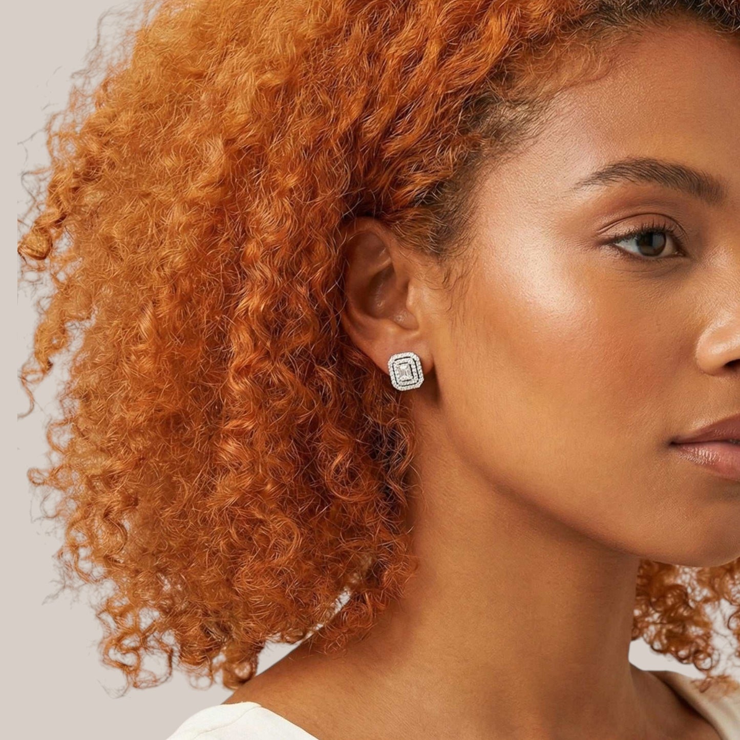 Woman with curly orange hair wearing a silver earring on a neutral background