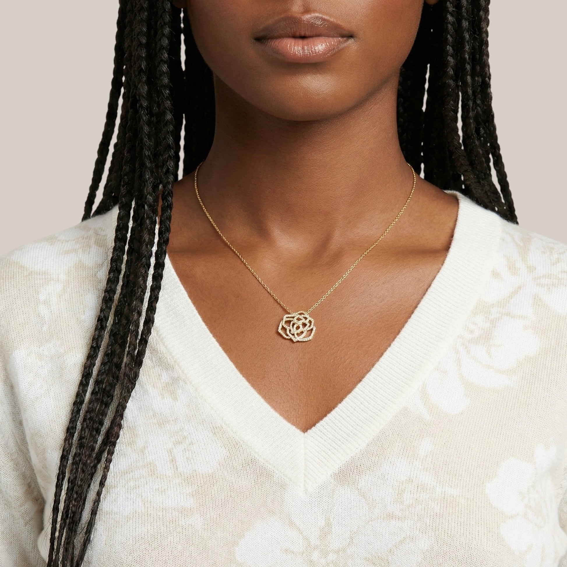 Woman wearing a gold necklace with a white sweater on a neutral background