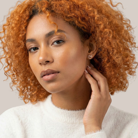Woman with curly orange hair touching her ear against a neutral background