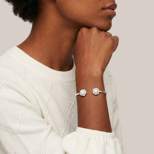 Person wearing a silver bracelet with two clear stones on a neutral background