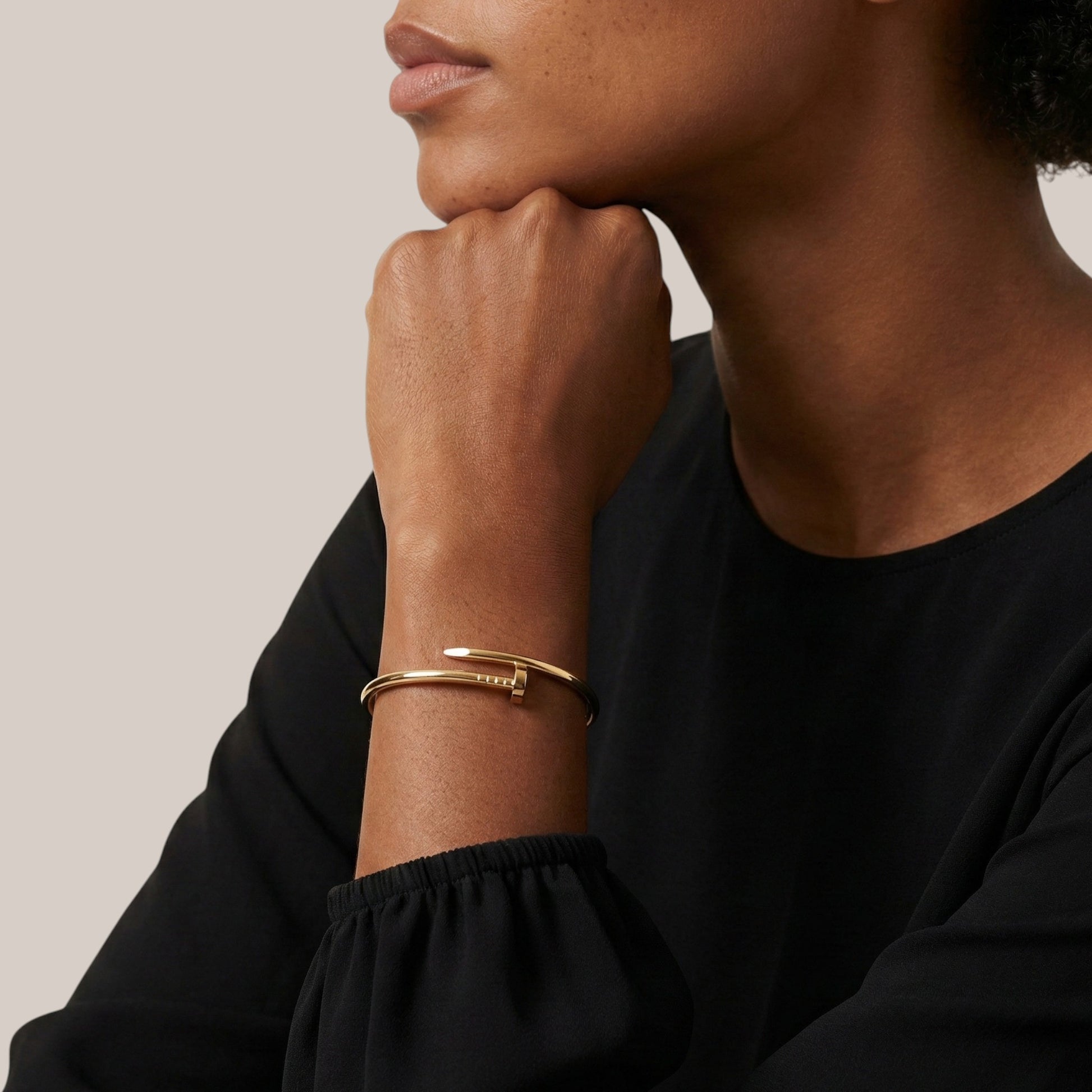 Person wearing a gold bracelet on a neutral background