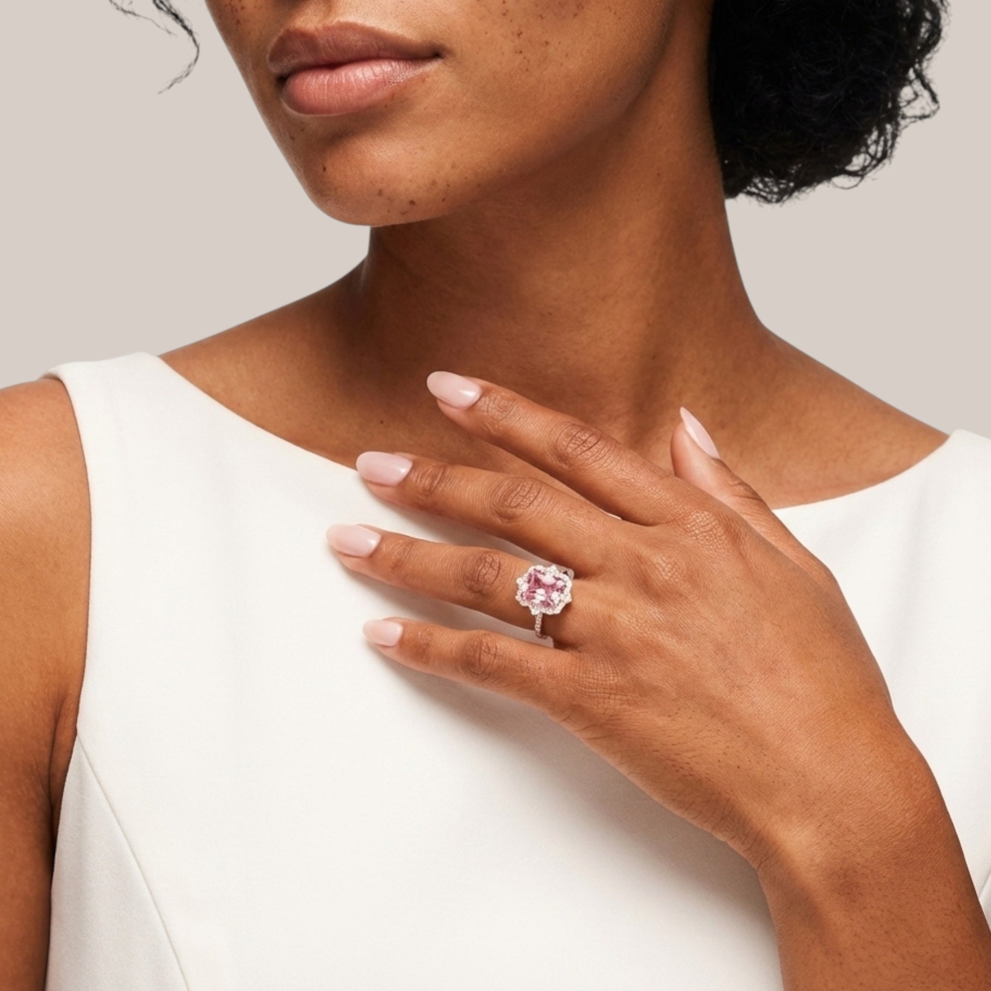 Woman wearing a pink gemstone ring on her hand against a neutral background