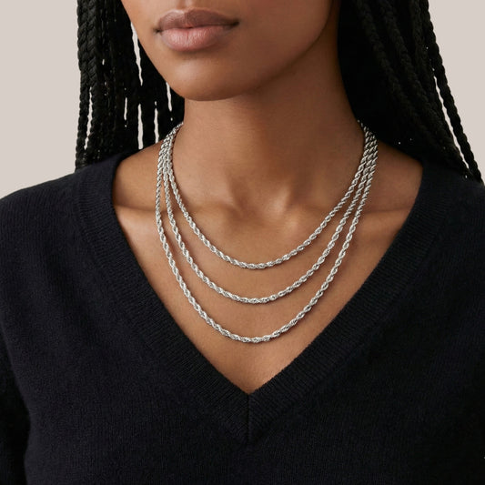 Woman wearing a stack of silver necklaces against a neutral background