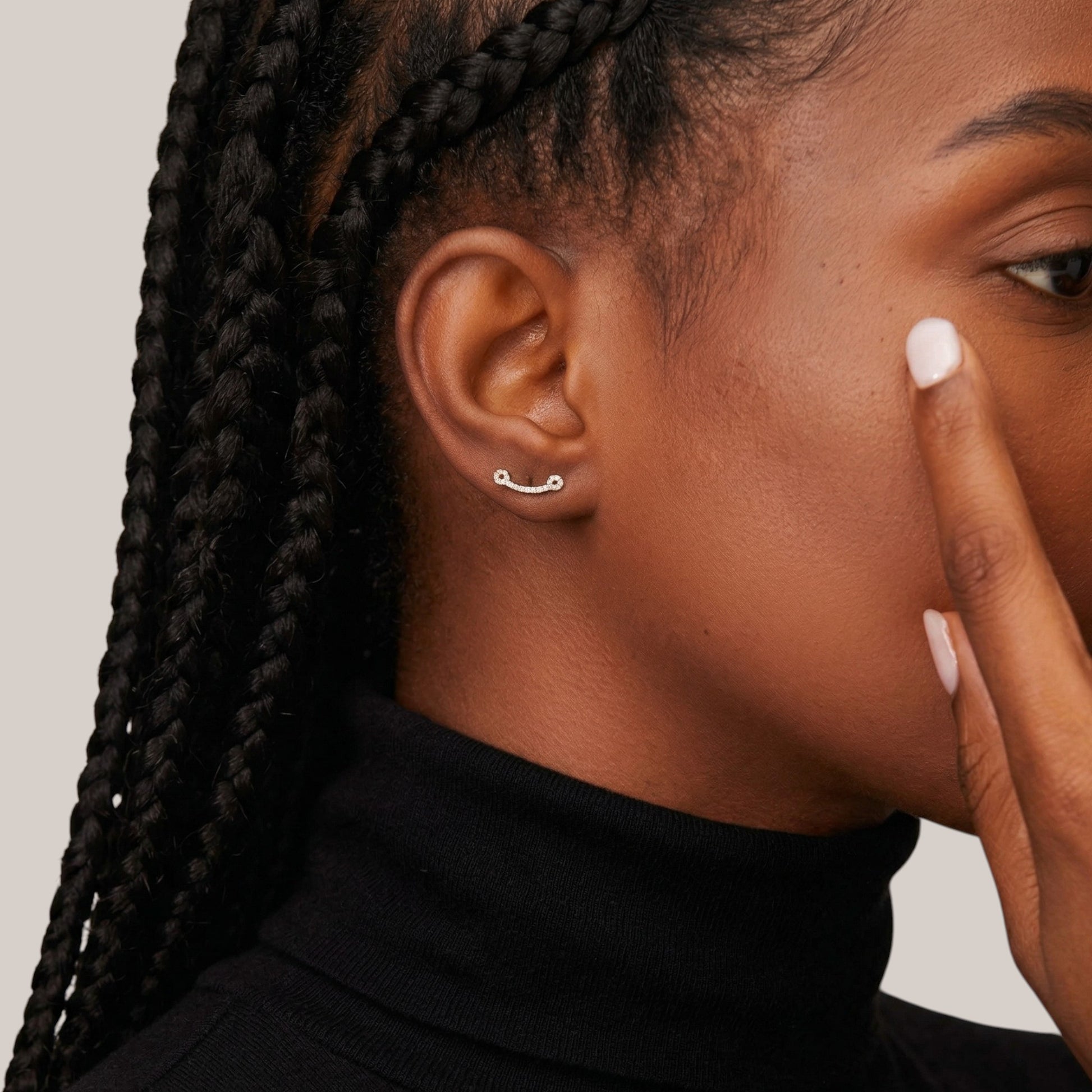 Close-up of a person with braided hair wearing a black turtleneck against a neutral background