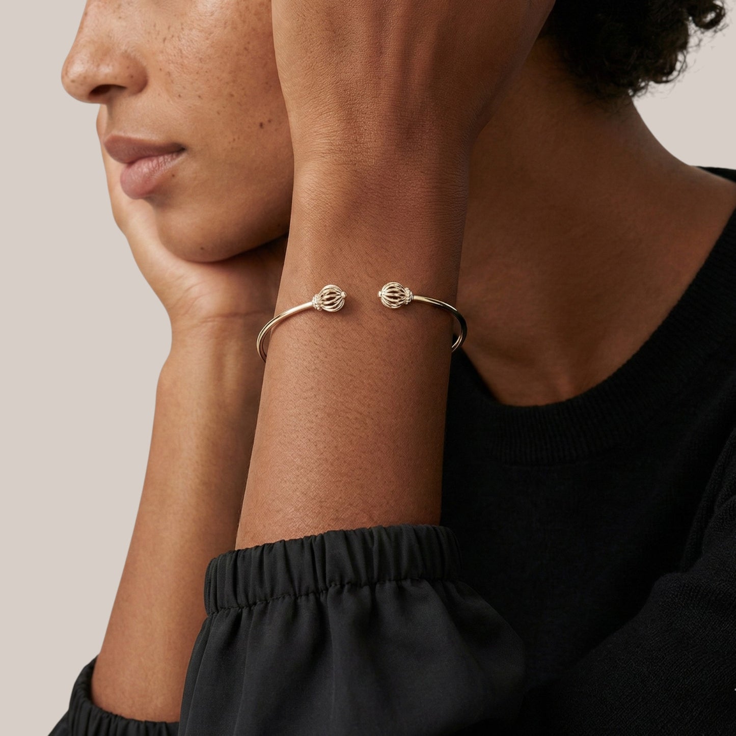 Close-up of a person wearing two gold bracelets on a neutral background