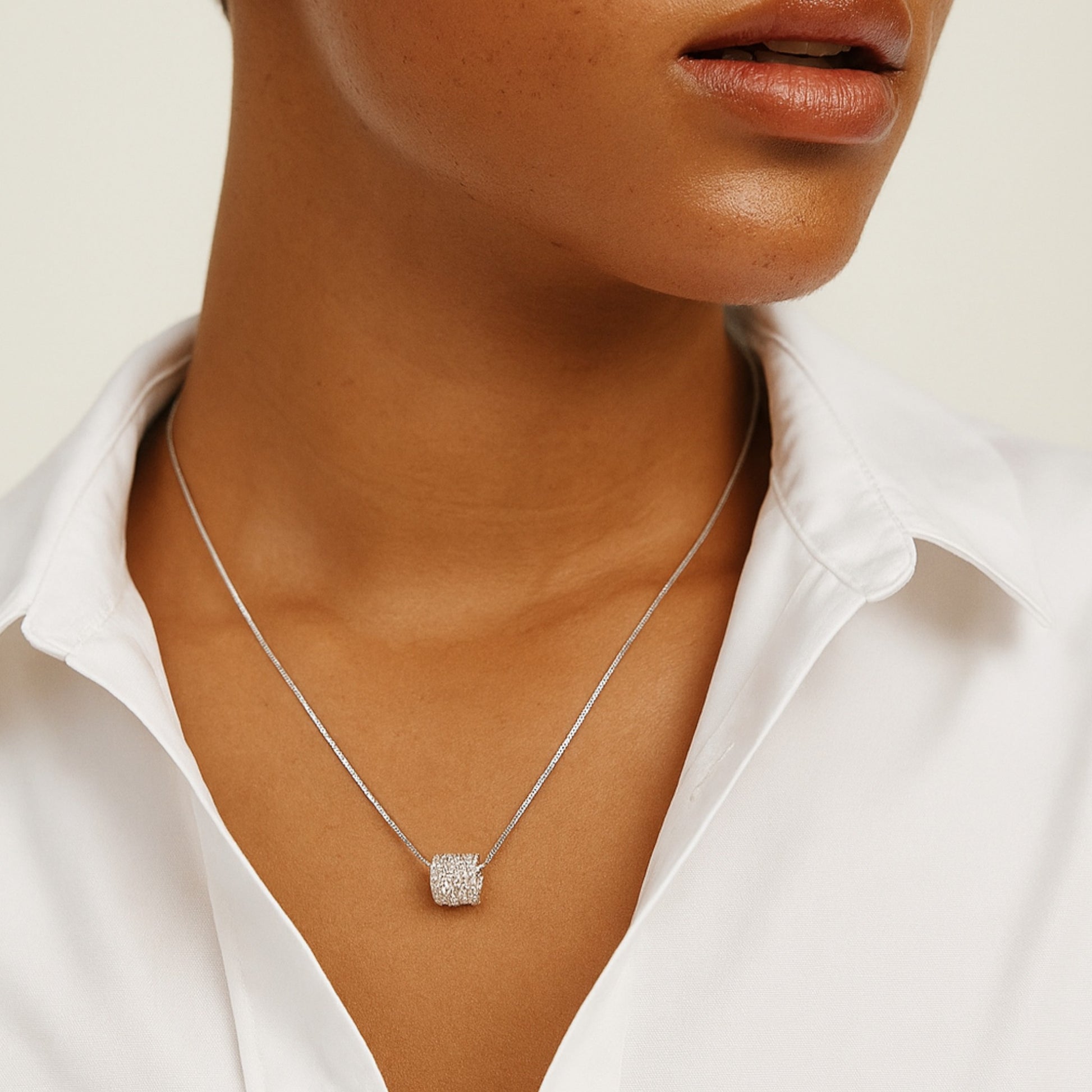 Silver necklace with a square pendant worn by a person in a white shirt.