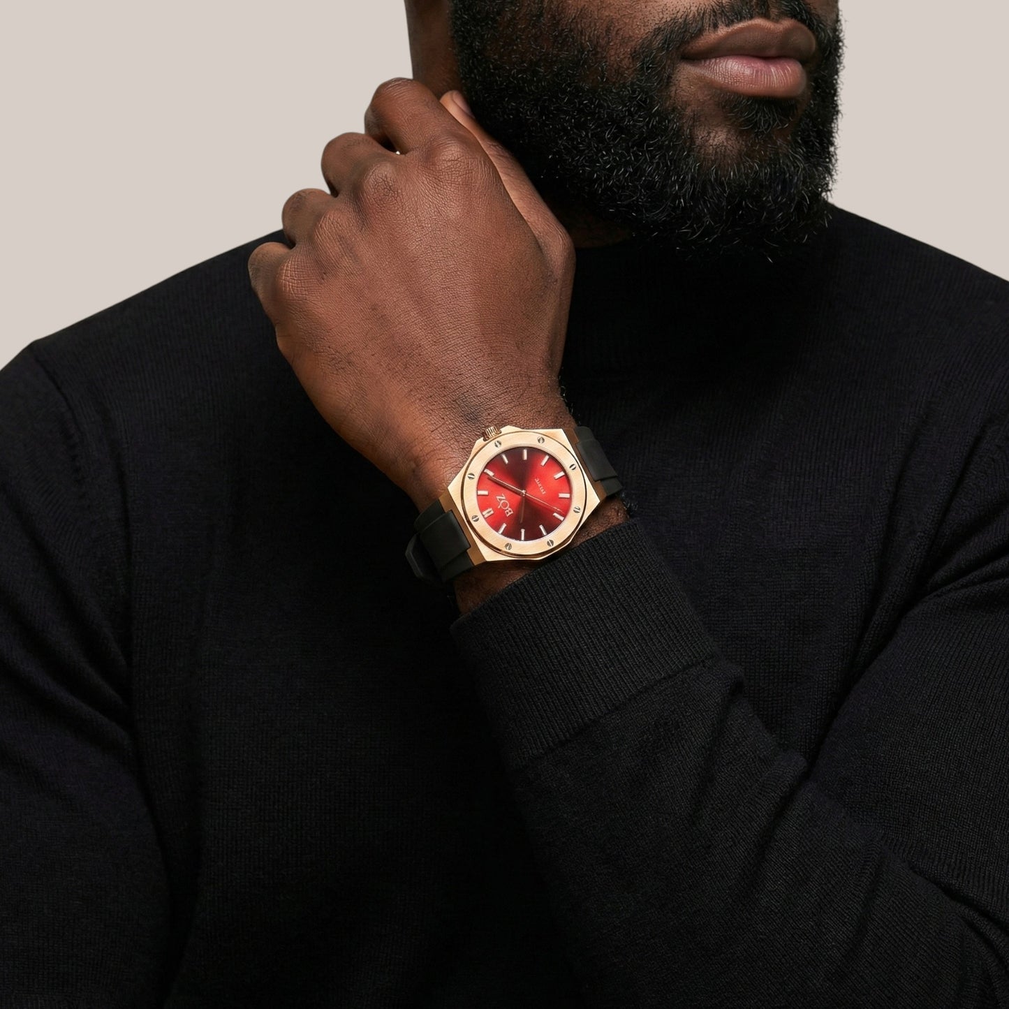 Man wearing a gold watch with a red face on a plain background