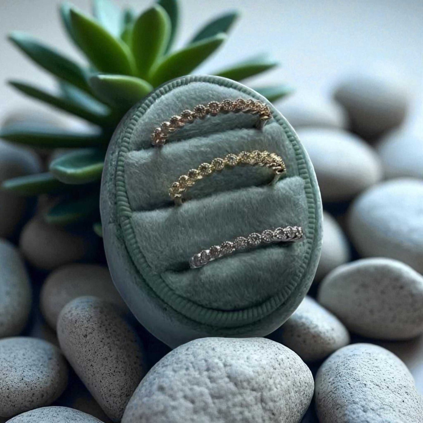 Set of gold rings on a green velvet stand with succulent and stones in the background