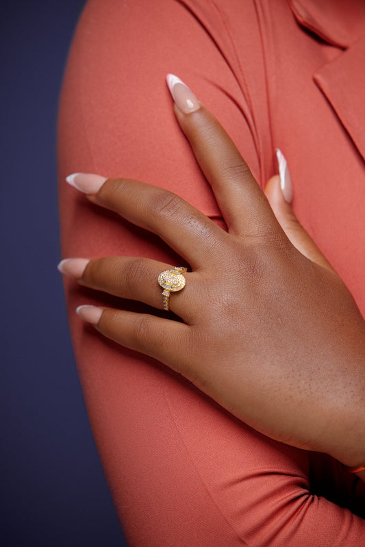 Hand wearing a gold ring on a pink garment against a dark background
