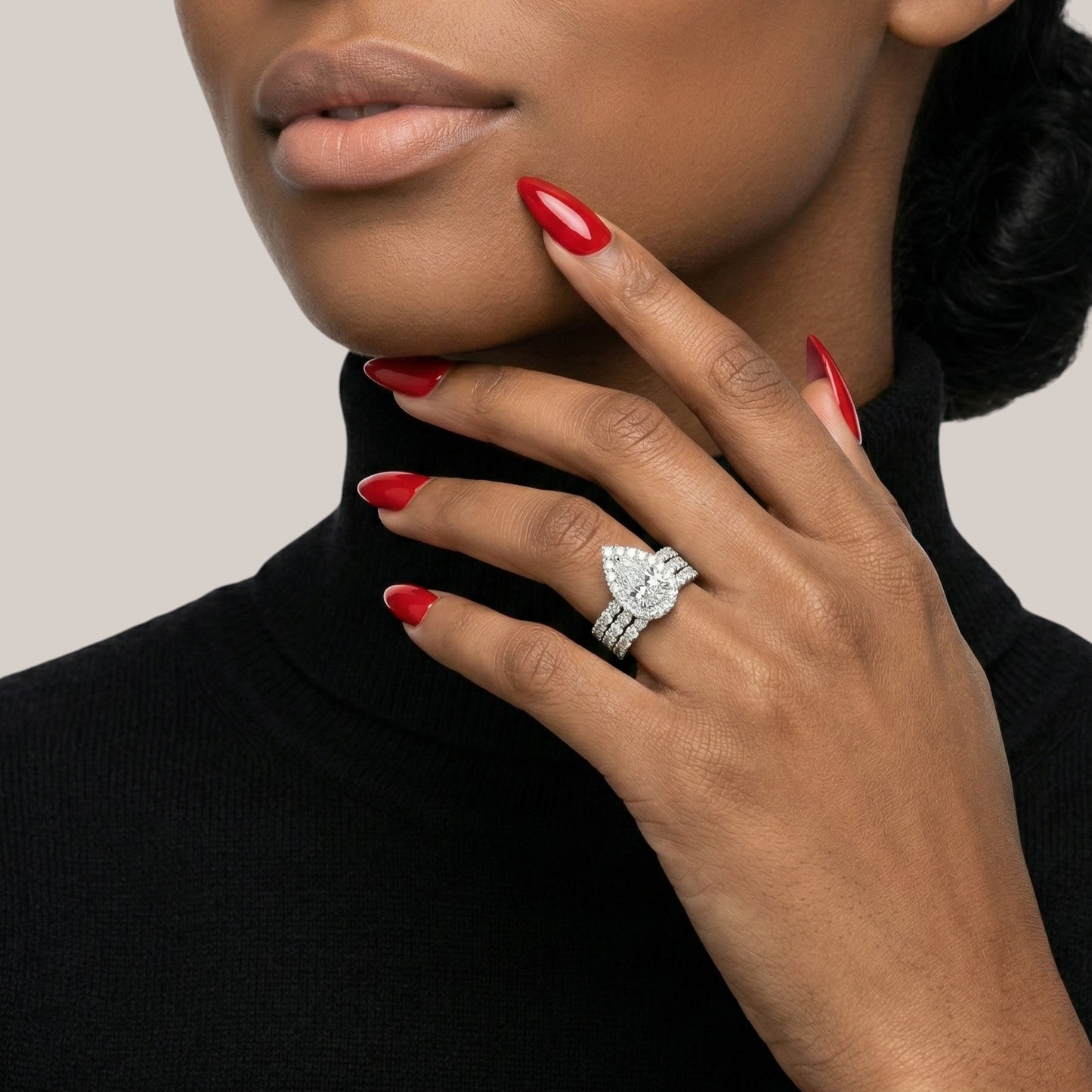 Woman wearing a diamond ring with red nail polish on a neutral background