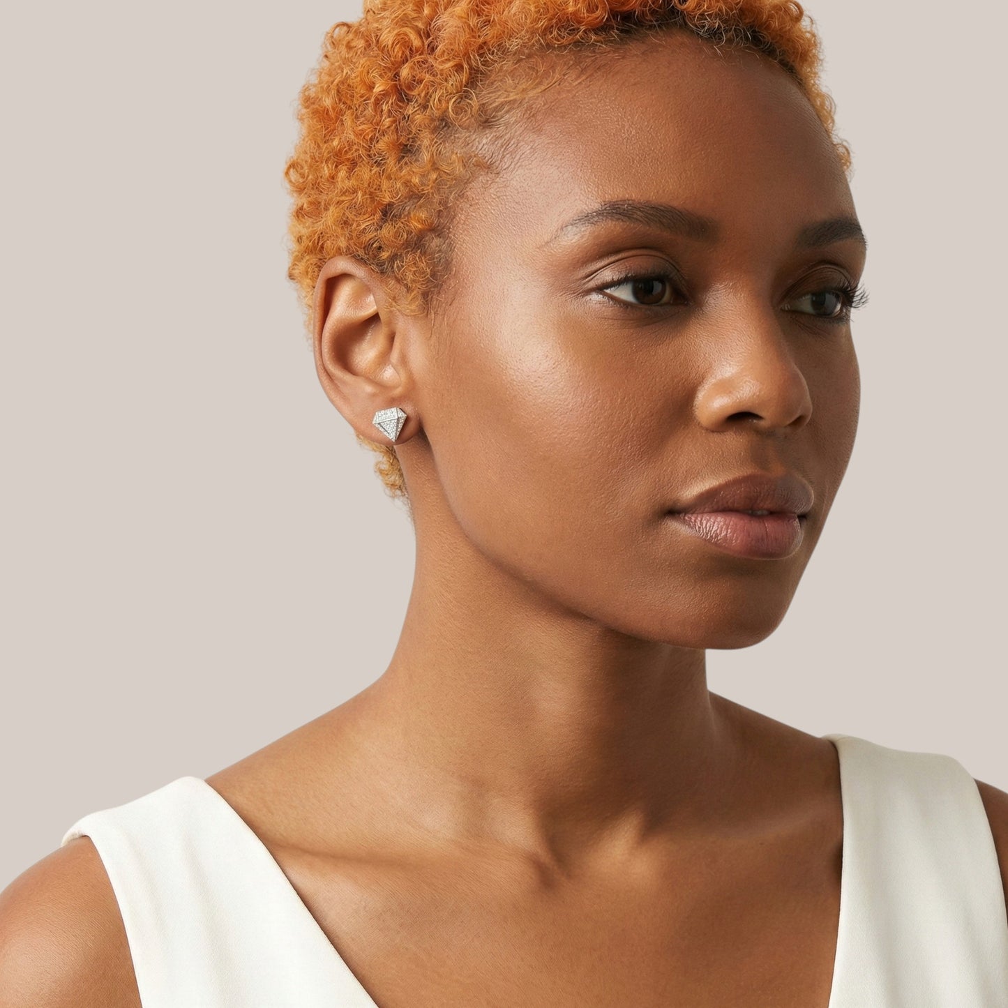 Woman with short, styled hair wearing a white sleeveless top against a neutral background