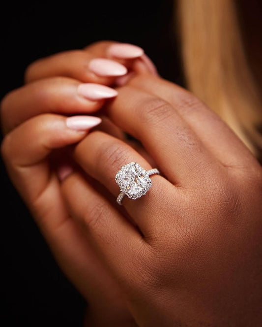 A person's hand holding a sparkling engagement ring with a 10 karat gold band.