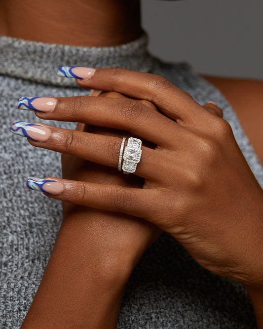 A close-up image of a person's hand showcasing an 18K gold engagement ring with a trinity baguette cut and natural diamond.