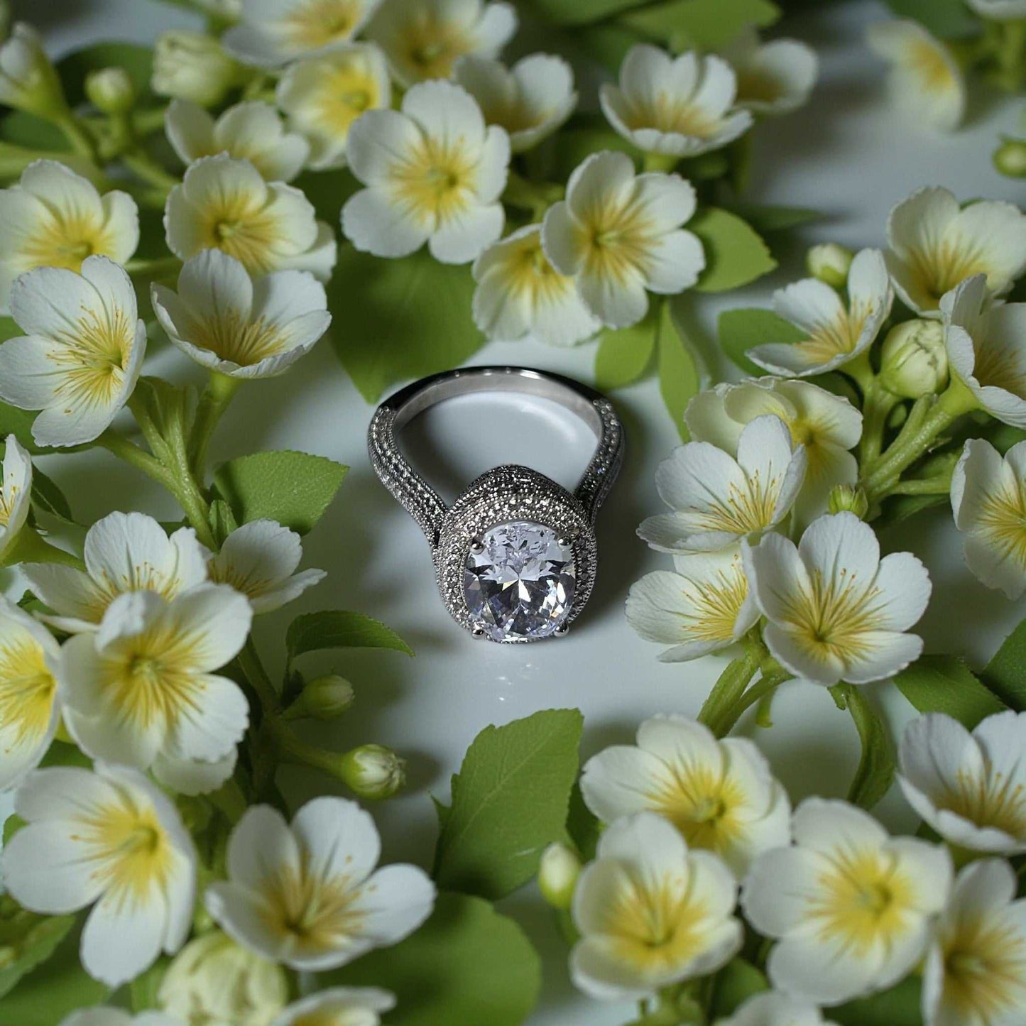 Zack Oval Cut CZ Engagement Ring in 925 sterling silver with oval cubic zirconia surrounded by micro pave detailing displayed on white and yellow flowers