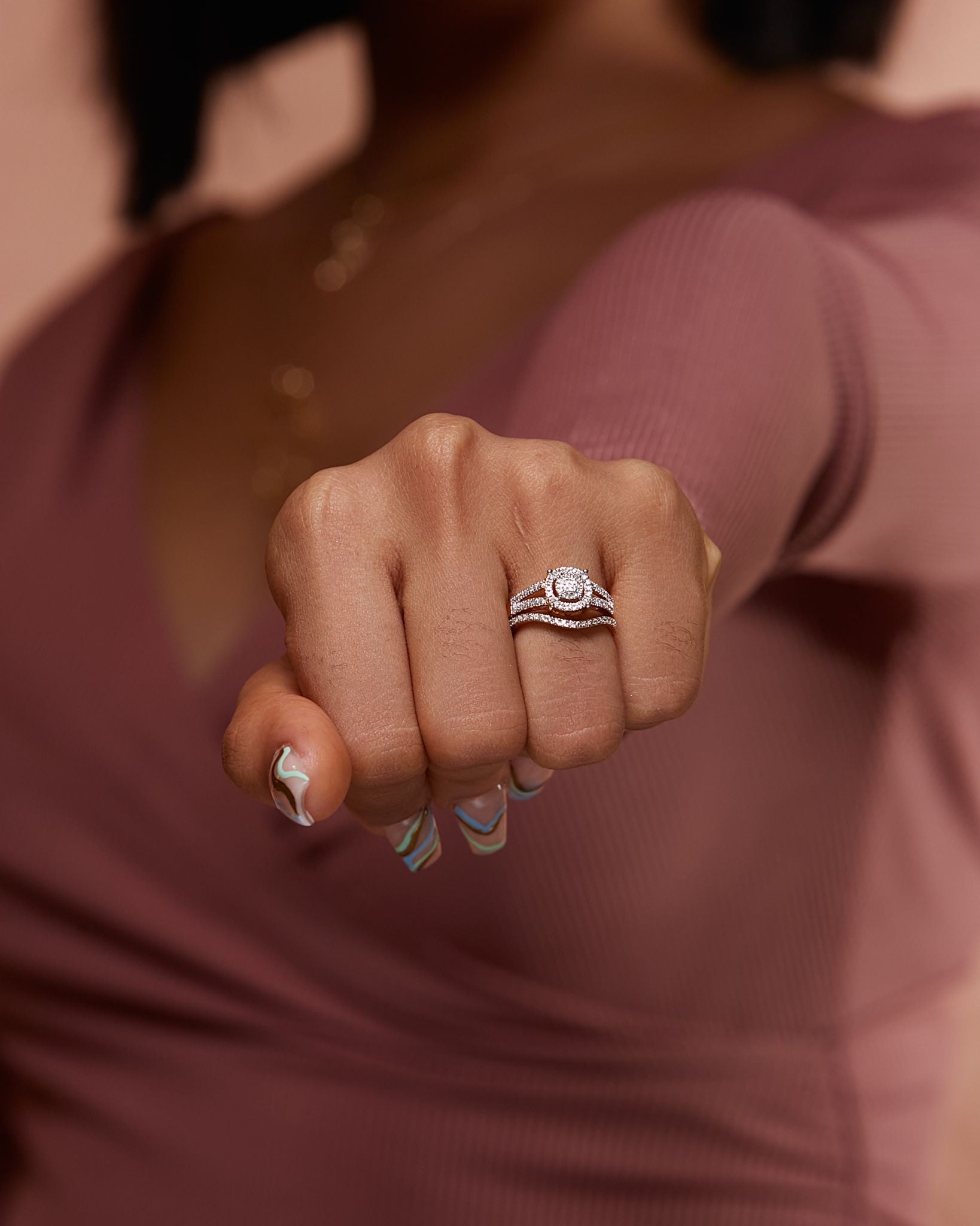 A close-up of a woman's hand wearing a round cut diamond cluster ring with 18 karat gold band.