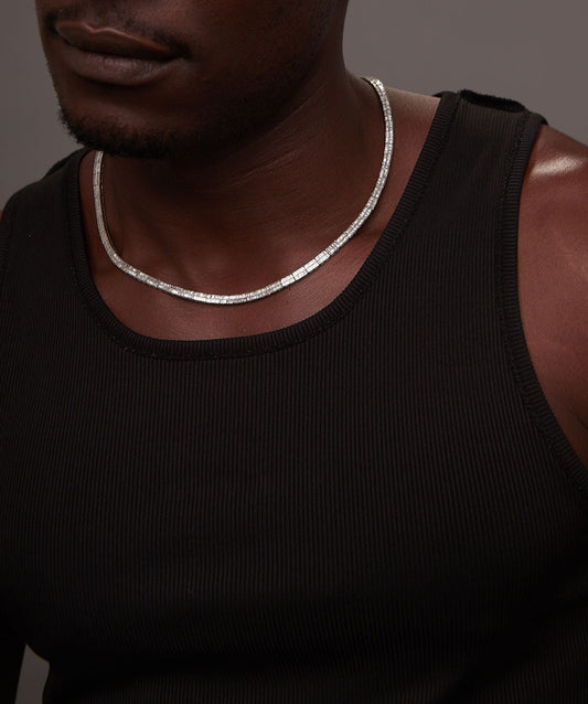 Man wearing a black tank top and silver necklace against a dark background