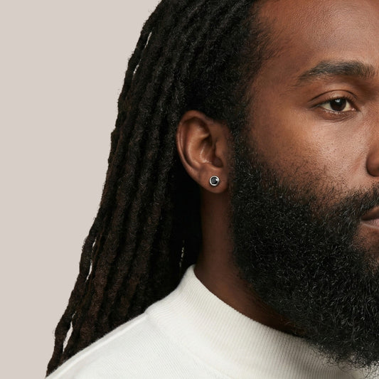 Close-up of a man with dreadlocks and a beard wearing a white shirt against a beige background