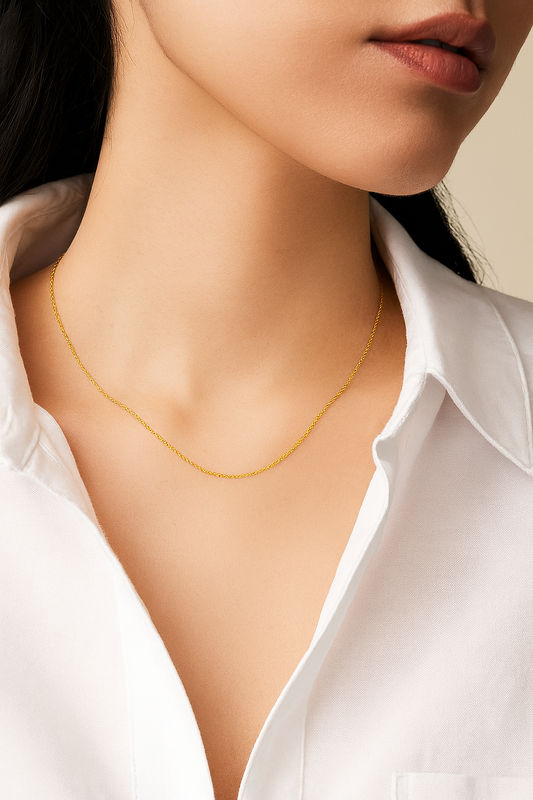 Close-up of a person wearing a delicate gold necklace with a white shirt.