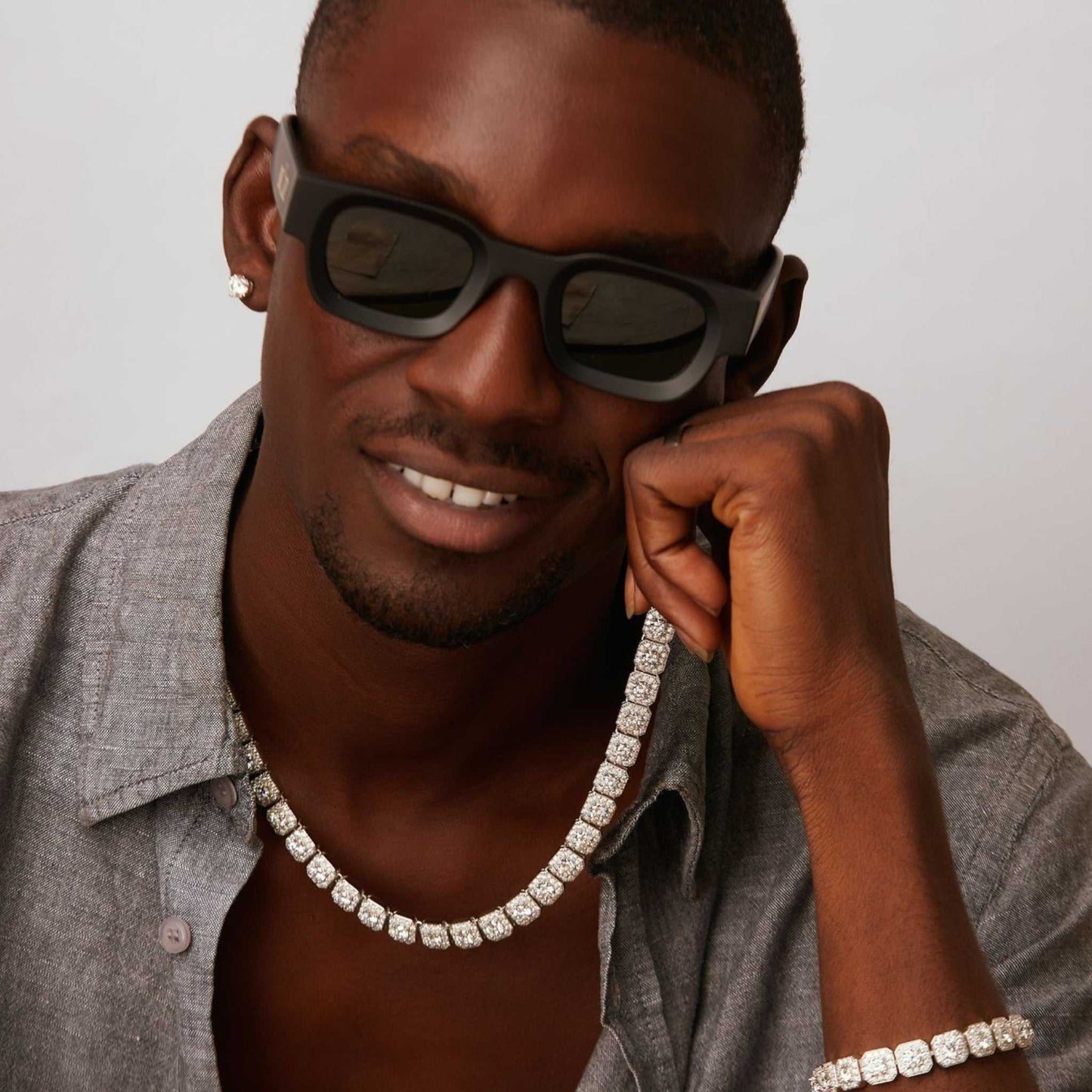 Man wearing sunglasses and a gray jacket with a diamond chain necklace.