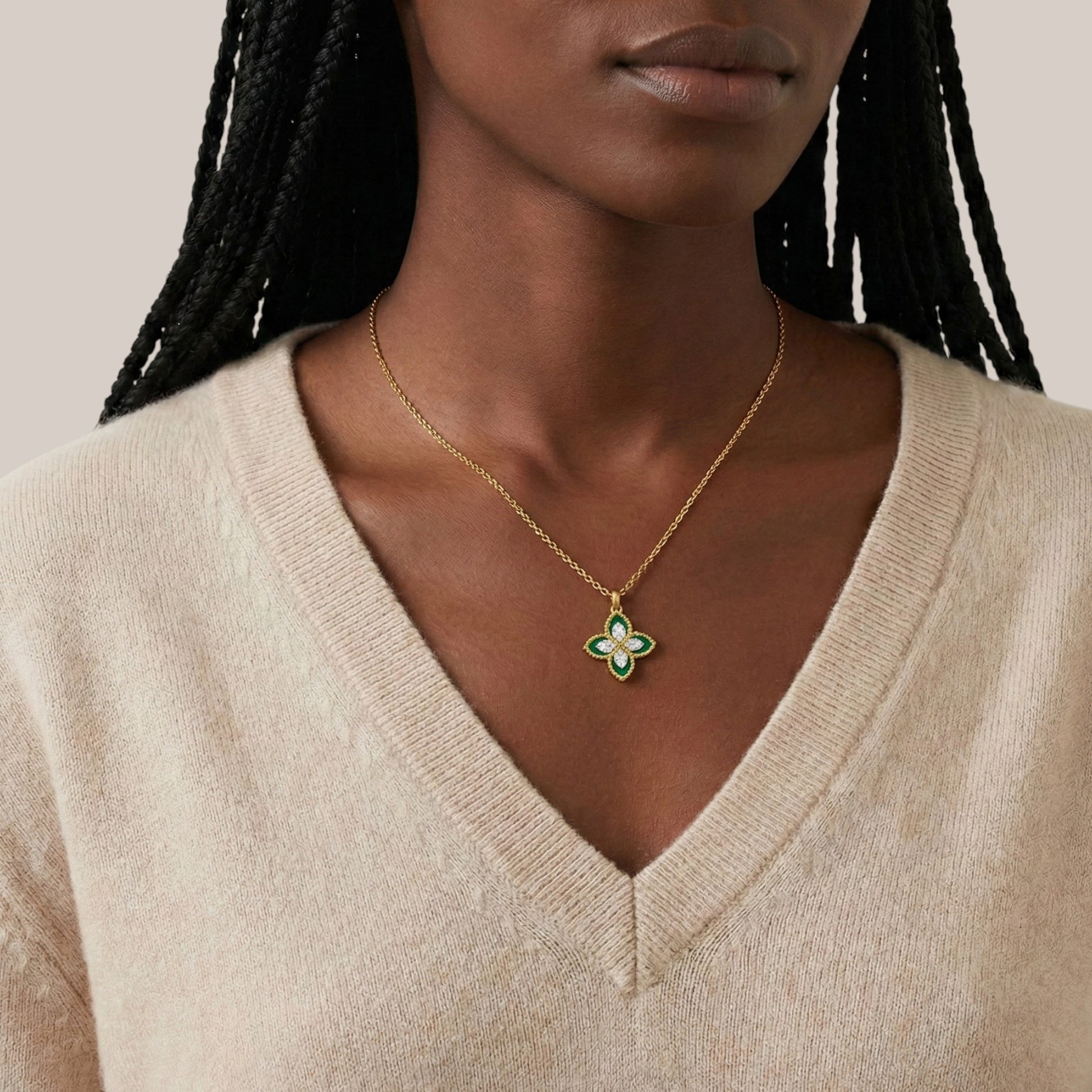 Woman wearing a gold necklace with a green pendant against a neutral background