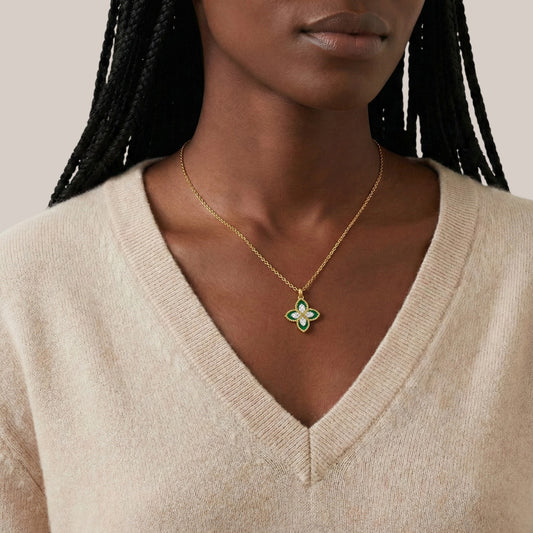 Woman wearing a gold necklace with a green pendant against a neutral background