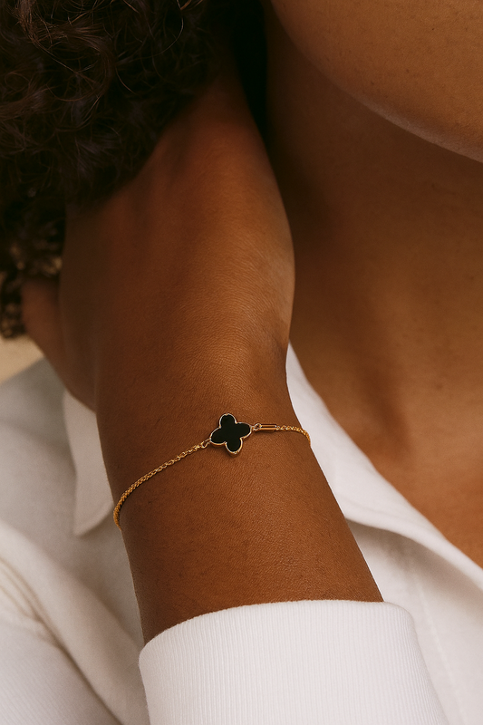 Close-up of a person wearing a gold bracelet with a clover charm on a white background