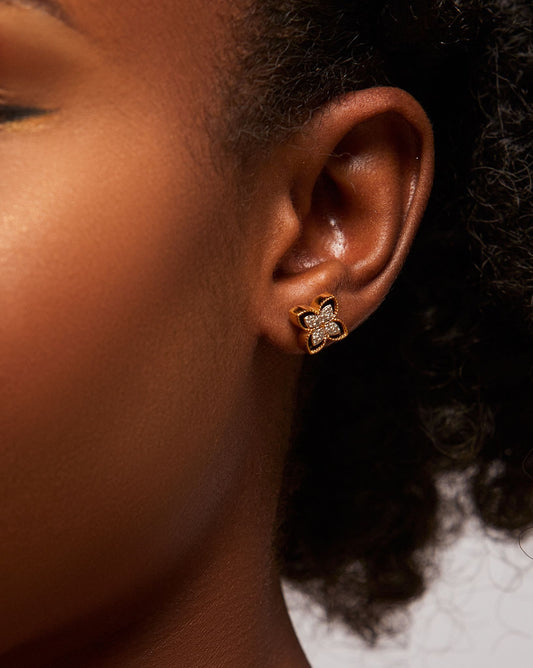A close-up image of a woman's ear wearing a gold-colored stud earring with a decorative element on the top.