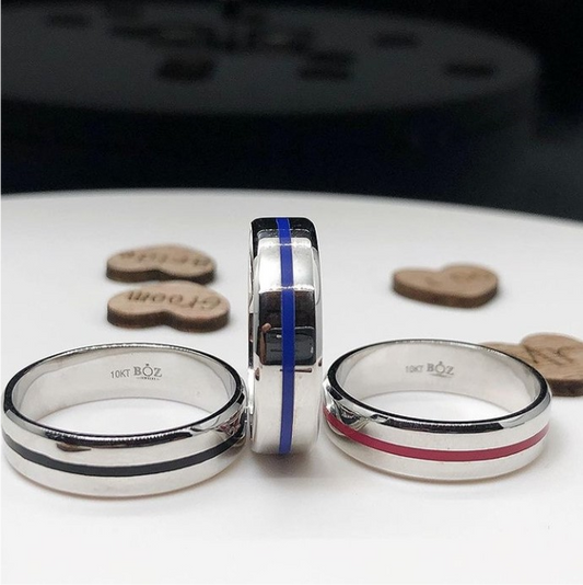 Two men's diamond rings with enamel lines, one in silver and one in gold color, displayed on a white surface, surrounded by small wooden discs.